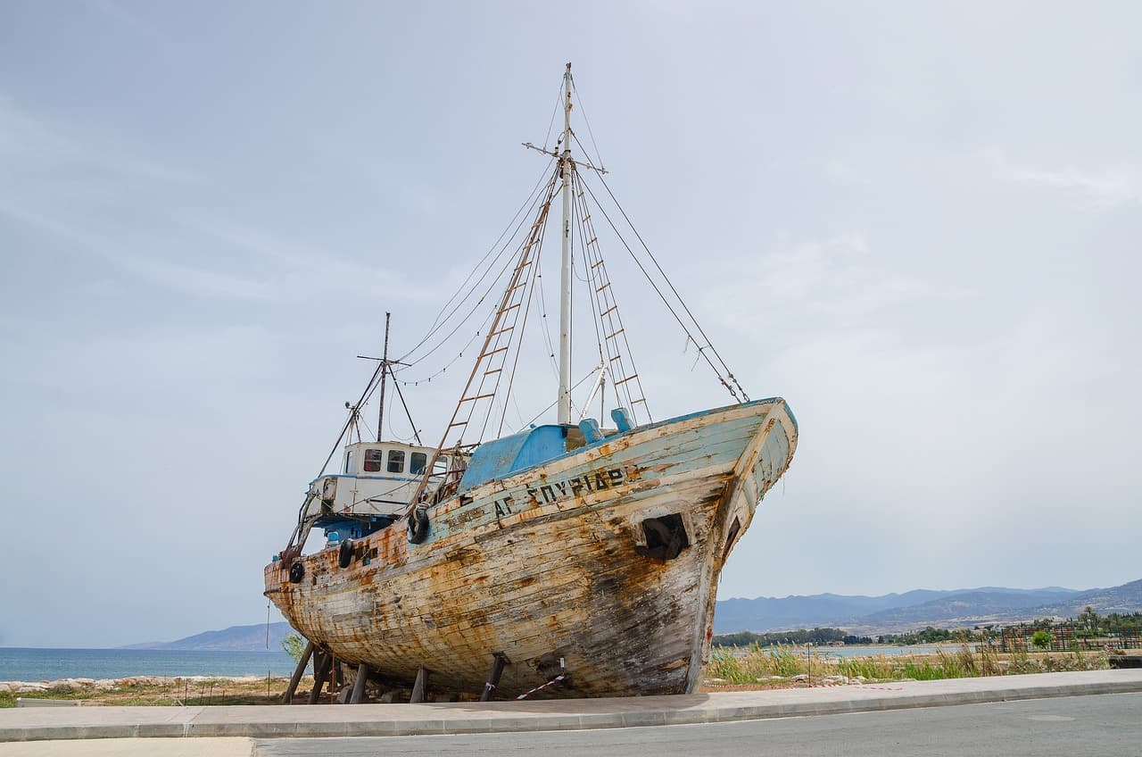 A weathered fishing boat on the quay at Latchi harbour with hills behind