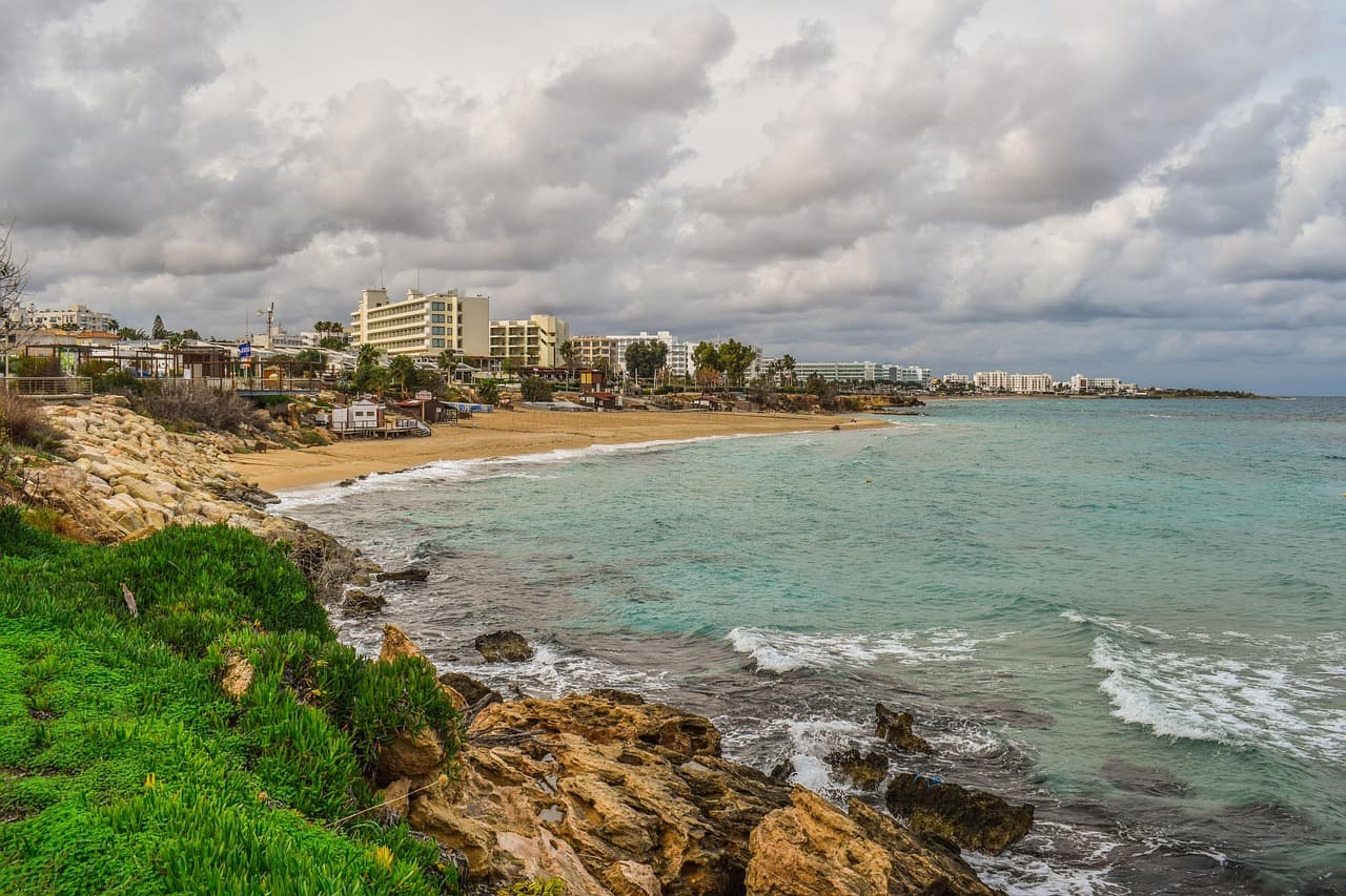 A bay with a sandy beach and hotels in the distance at Protaras